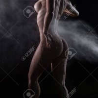 Naked Female Figure In The Shower. Wet Woman Without Clothes With A Beautiful Figure Under The Streams Of Water From A Spray Bottle. Drops Flow Down On A Perfect Bare Chest And