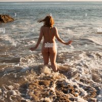Rear view of naked mid adult woman running into the sea on El Matador Beach Malibu California USA Stock Photo